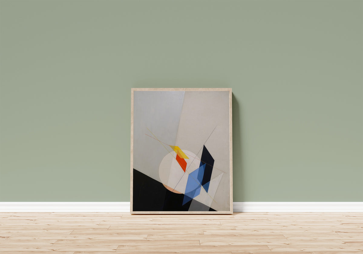Framed art print of A 18 by László Moholy-Nagy, in a light wood frame leaning on a sage green wall above a wooden floor