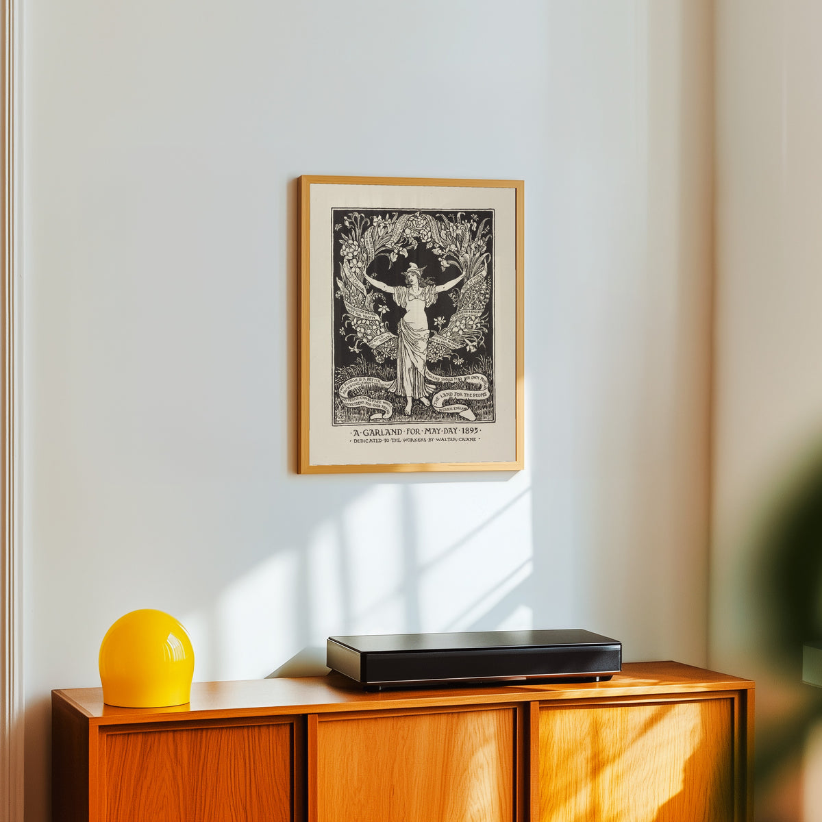 Framed art print of A Garland for May Day by Walter Crane, in a light wood frame on a white wall above an orange sideboard