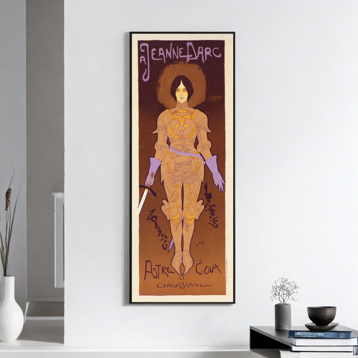Framed art print of A Jeanne d'Arc by Georges de Feure, on a white wall above books and a bowl