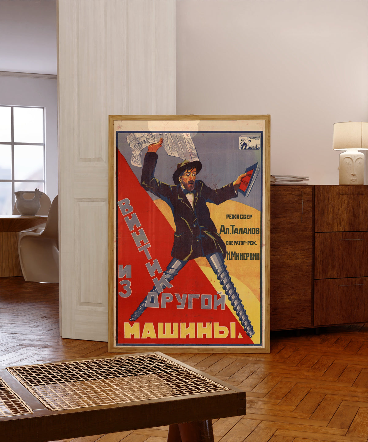 Framed art print of A Screw from Another Machine, in a light wood frame leaning in a warm room with a parquet floor