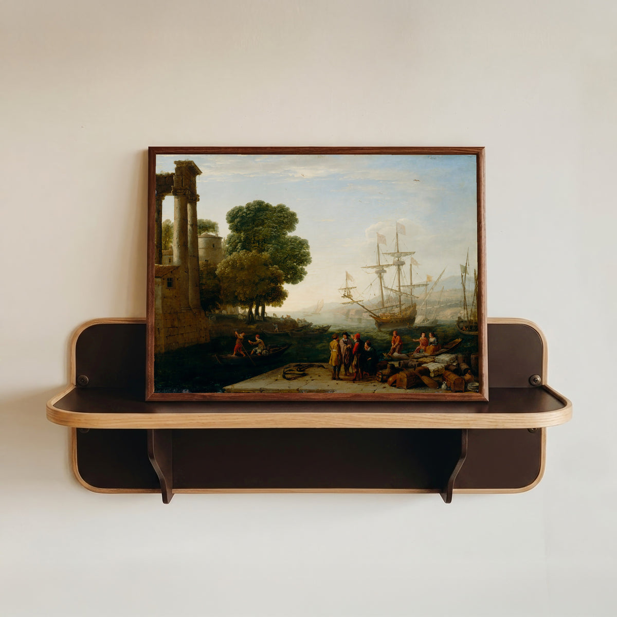 Framed art print of A Seaport at Sunset by Claude Lorrain, in a dark wood frame resting on a wall shelf