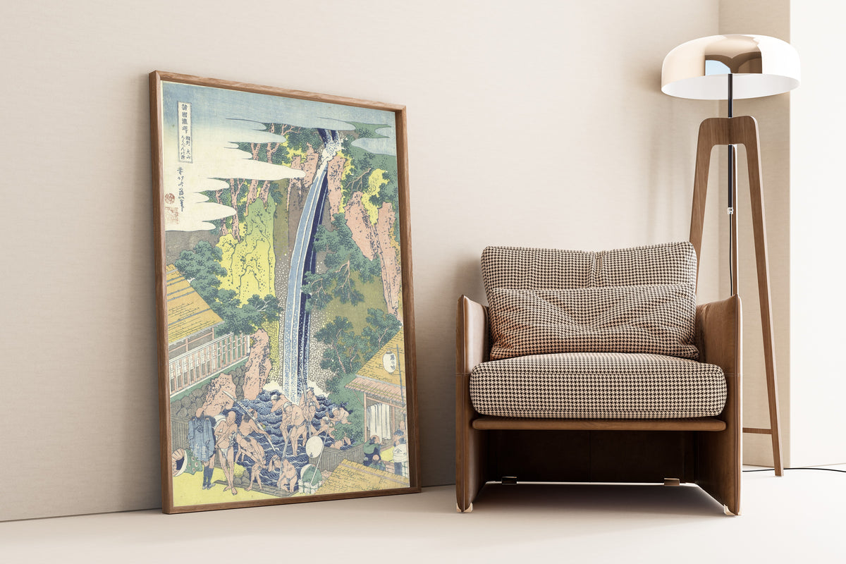 Framed art print of A Tour of the Waterfalls of the Provinces: Rōben… by Katsushika Hokusai, leaning against a wall beside an armchair and a floor lamp