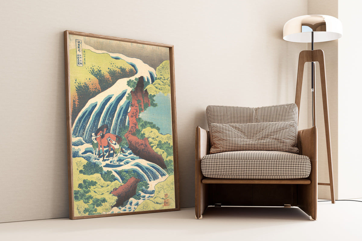 Framed art print of A Tour of the Waterfalls of the Provinces: The Waterfall… by Katsushika Hokusai, leaning against a wall beside an armchair and a floor lamp