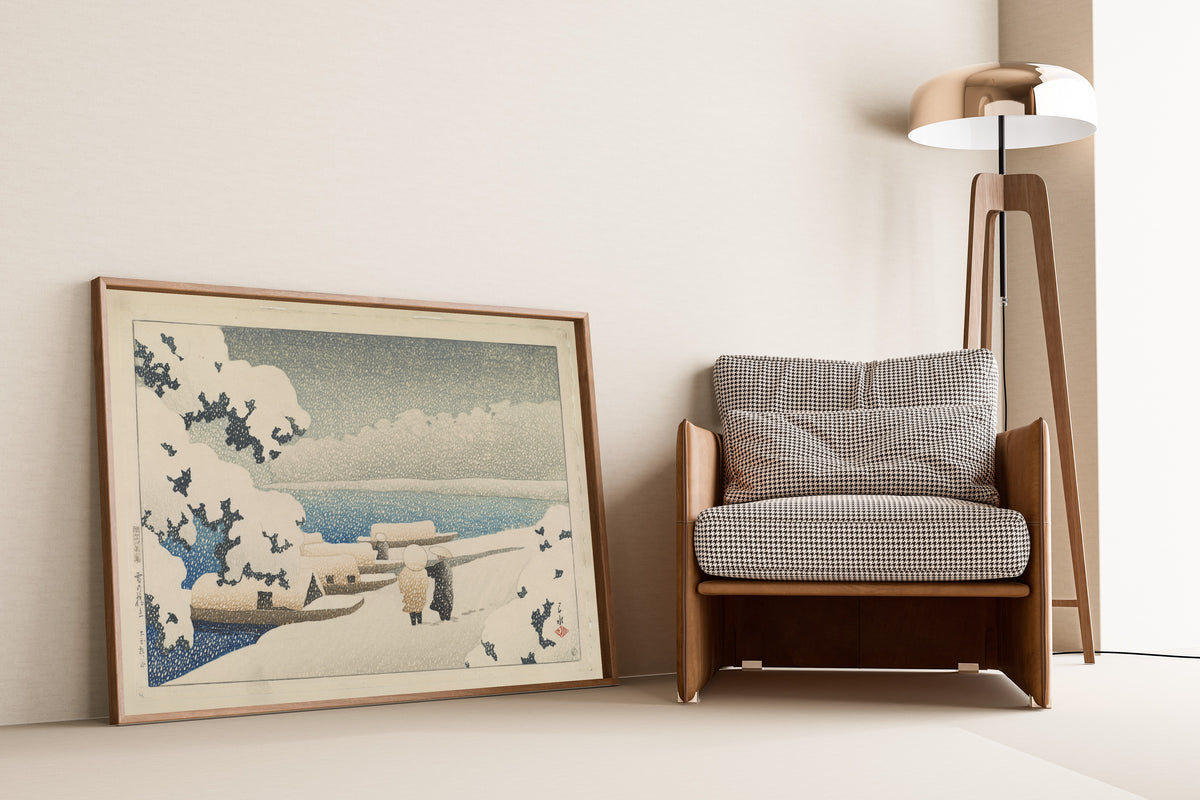 Framed art print of Amanohashidate in Snow by Kawase Hasui, leaning against a wall beside an armchair and a floor lamp