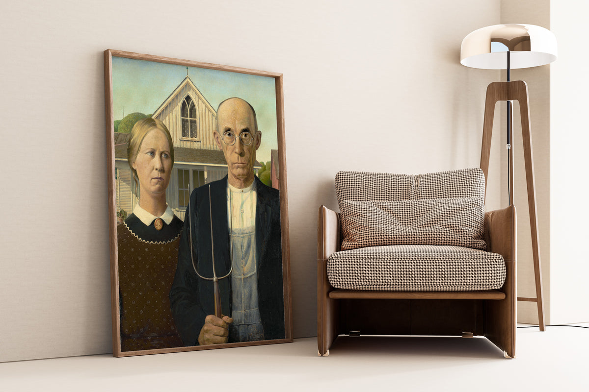 American Gothic by Grant Wood — framed and leaning against a wall beside an armchair and a floor lamp