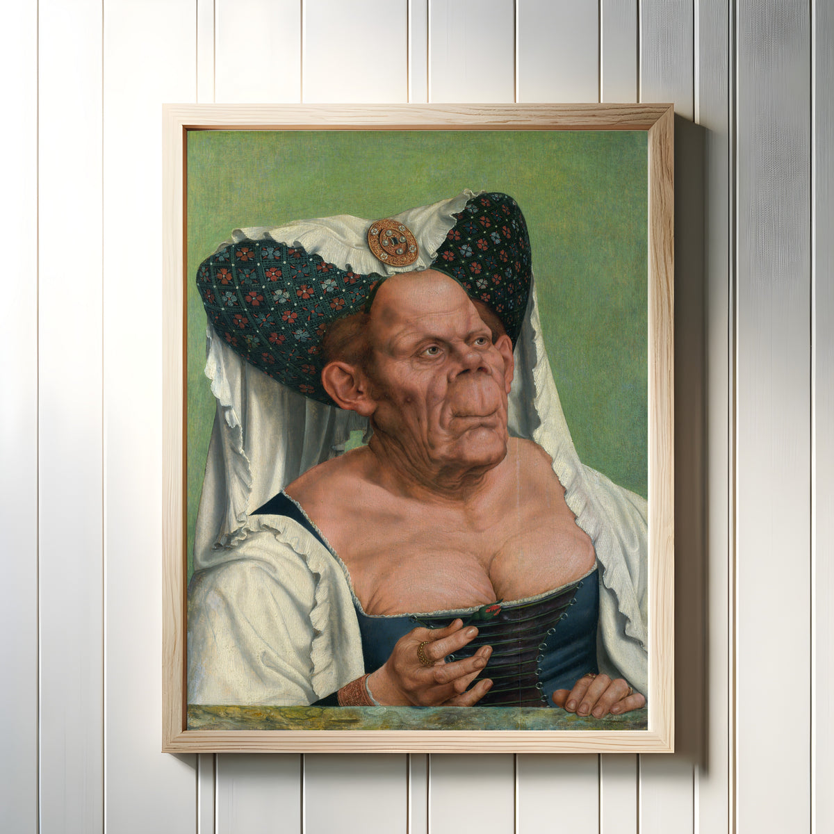 Framed art print of An Old Woman (The Ugly Duchess) by Quinten Massys, in a light wood frame on a white panelled wall