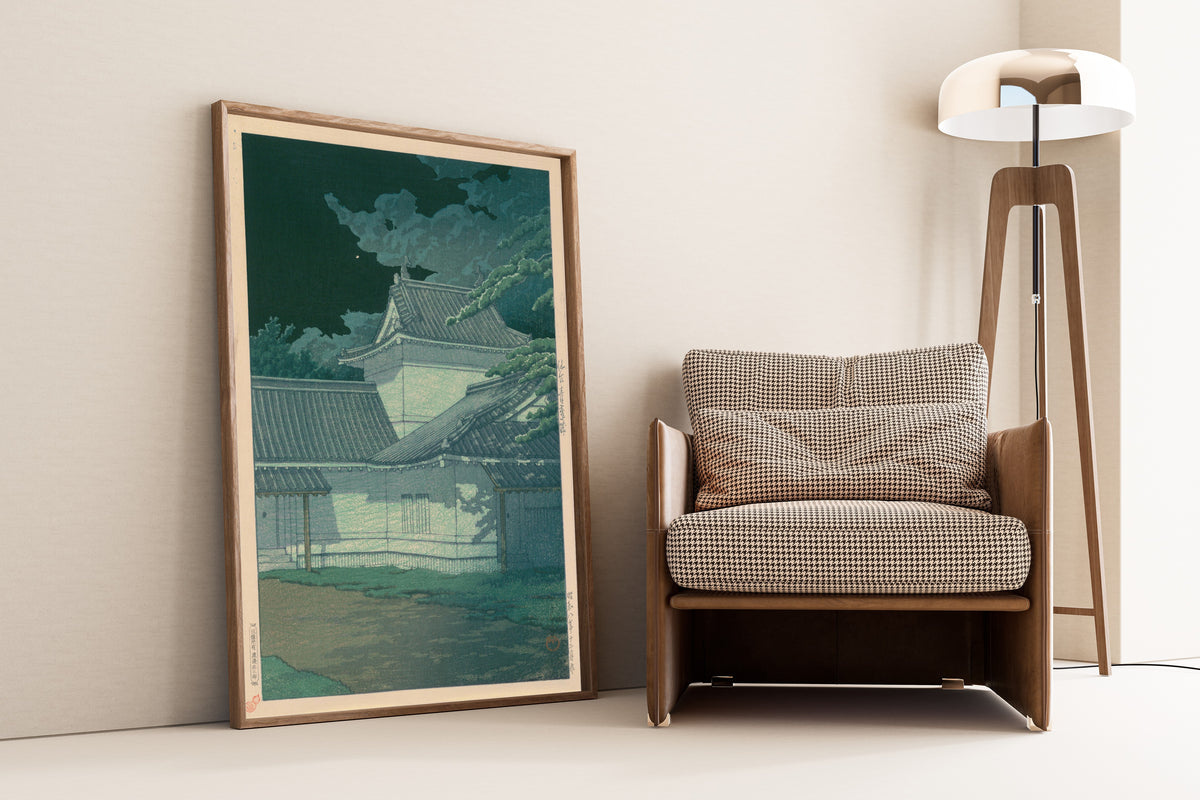 Framed art print of Aoba Castle, Sendai by Kawase Hasui, leaning against a wall beside an armchair and a floor lamp