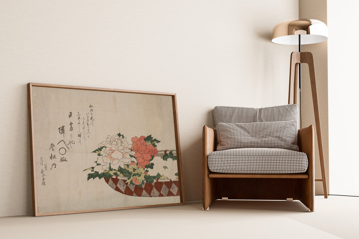 Framed art print of Basket of Peonies by Katsushika Hokusai, leaning against a wall beside an armchair and a floor lamp