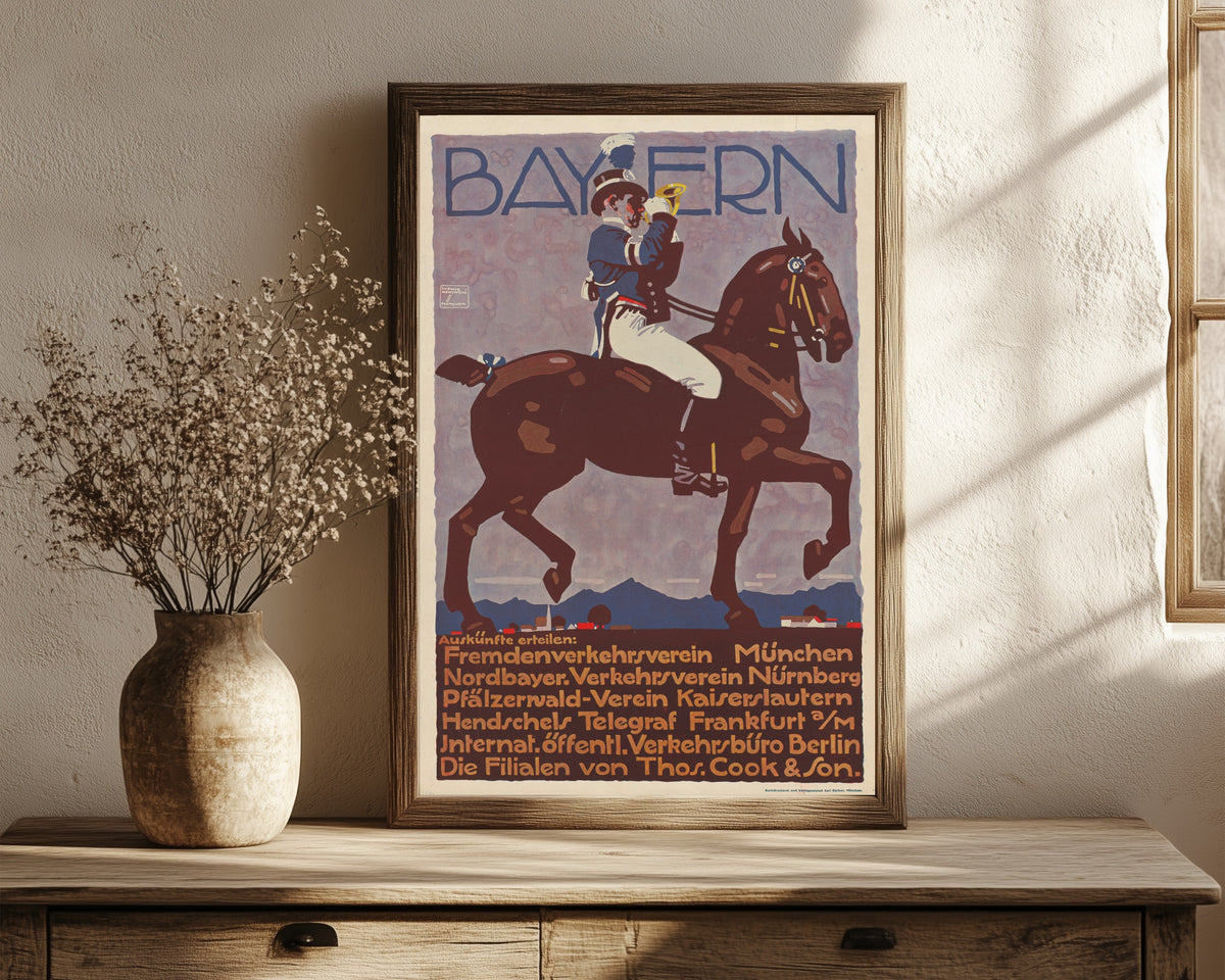 Framed art print of Bayern by Ludwig Hohlwein, in a dark wood frame leaning on a rustic console beside dried flowers