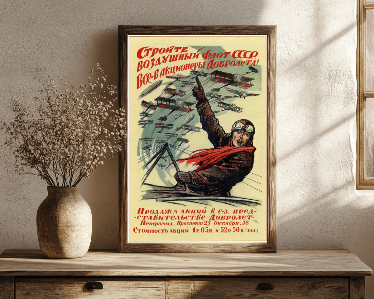Framed art print of Build the air fleet of the USSR! Everyone, become a… by Ivan Simakov, in a dark wood frame leaning on a rustic console beside dried flowers