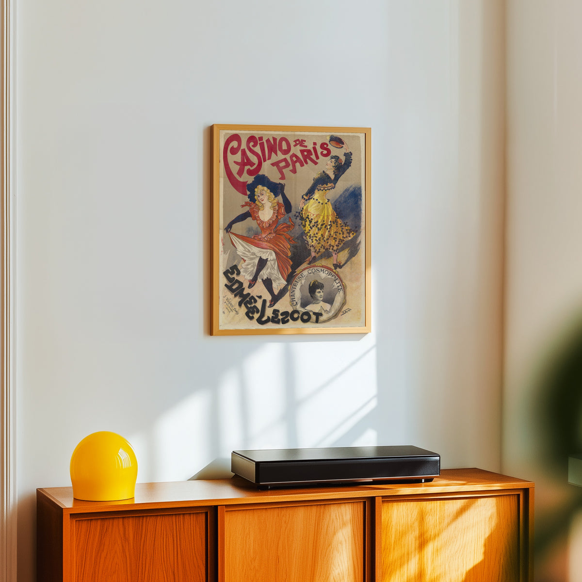 Framed art print of Casino de Paris: Edmée Lescot, chanteuse cosmopolite by Georges de Feure, in a light wood frame on a white wall above an orange sideboard