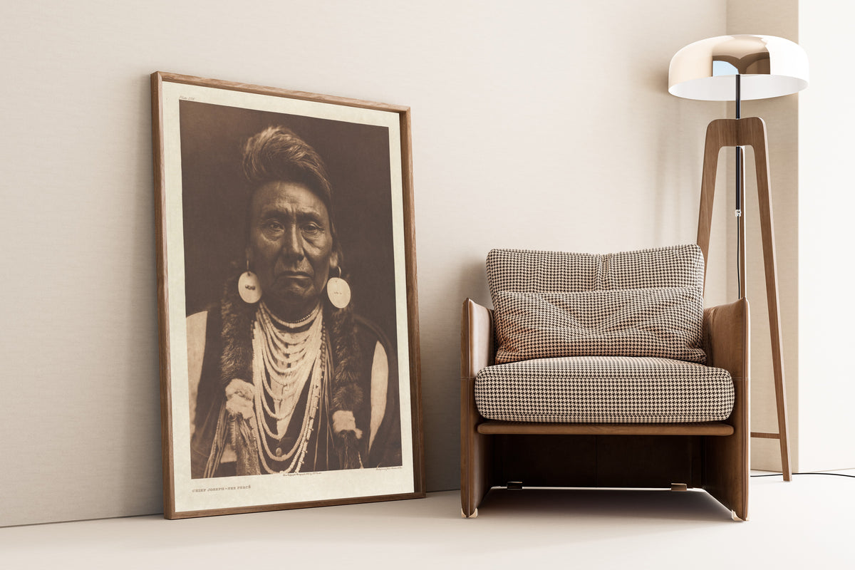 Framed art print of Chief Joseph, Nez Percé by Edward S. Curtis, leaning against a wall beside an armchair and a floor lamp