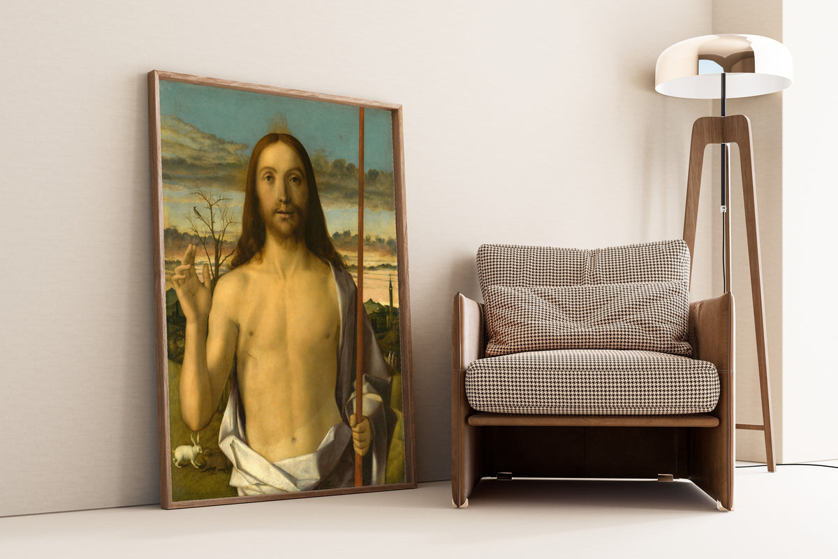Framed art print of Christ Blessing by Giovanni Bellini, leaning against a wall beside an armchair and a floor lamp