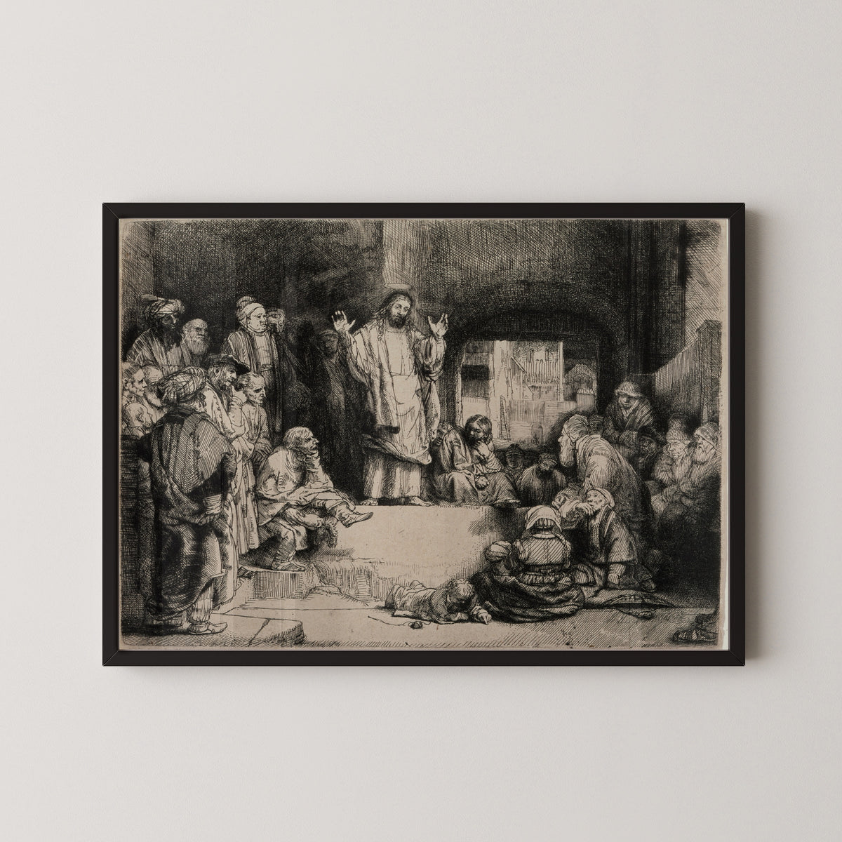 Framed art print of Christ Preaching, called La Petite Tombe by Rembrandt van Rijn, in a black frame on a pale wall