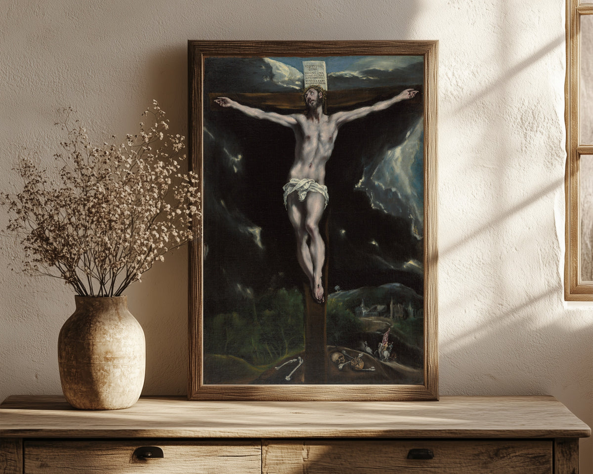 Framed art print of Christ on the Cross by El Greco, in a dark wood frame leaning on a rustic console beside dried flowers