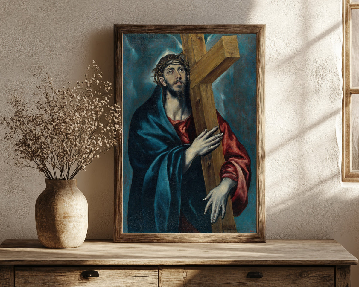 Framed art print of Christ with the Cross by El Greco, in a dark wood frame leaning on a rustic console beside dried flowers