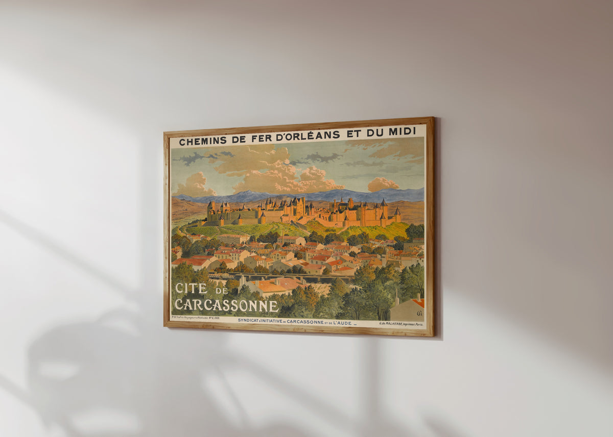 Framed art print of Cité de Carcassonne by Eugène Grasset, in a light wood frame on a sunlit white wall, seen at a slight angle