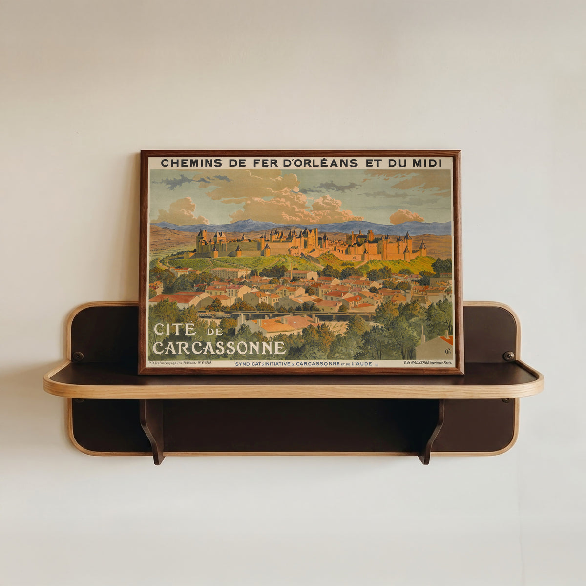 Framed art print of Cité de Carcassonne by Eugène Grasset, in a dark wood frame resting on a wall shelf