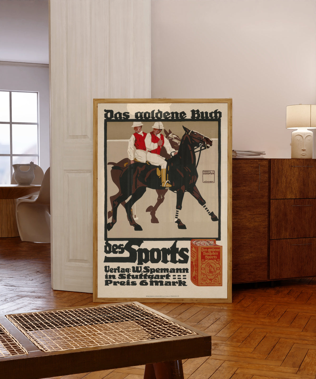 Framed art print of Das goldene Buch des Sports by Ludwig Hohlwein, in a light wood frame leaning in a warm room with a parquet floor