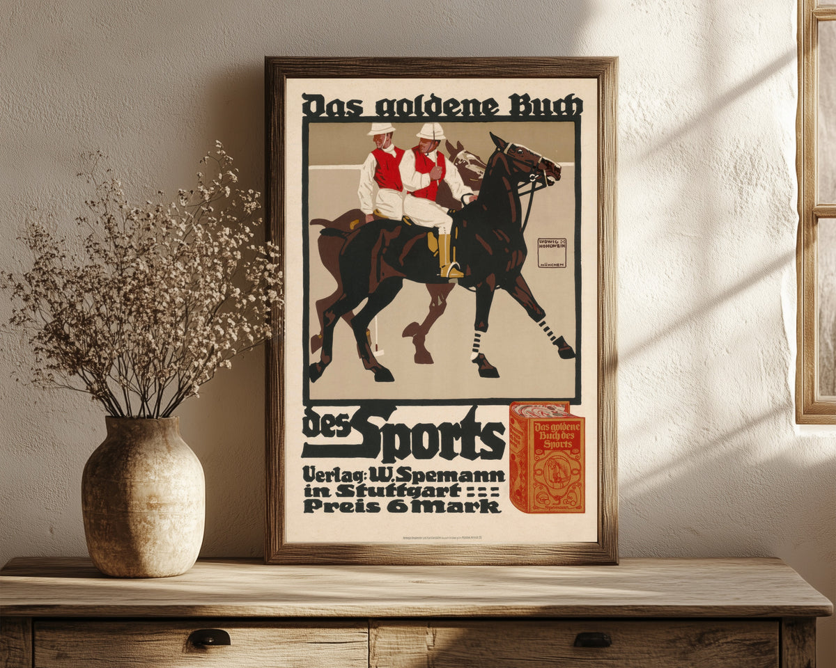 Framed art print of Das goldene Buch des Sports by Ludwig Hohlwein, in a dark wood frame leaning on a rustic console beside dried flowers