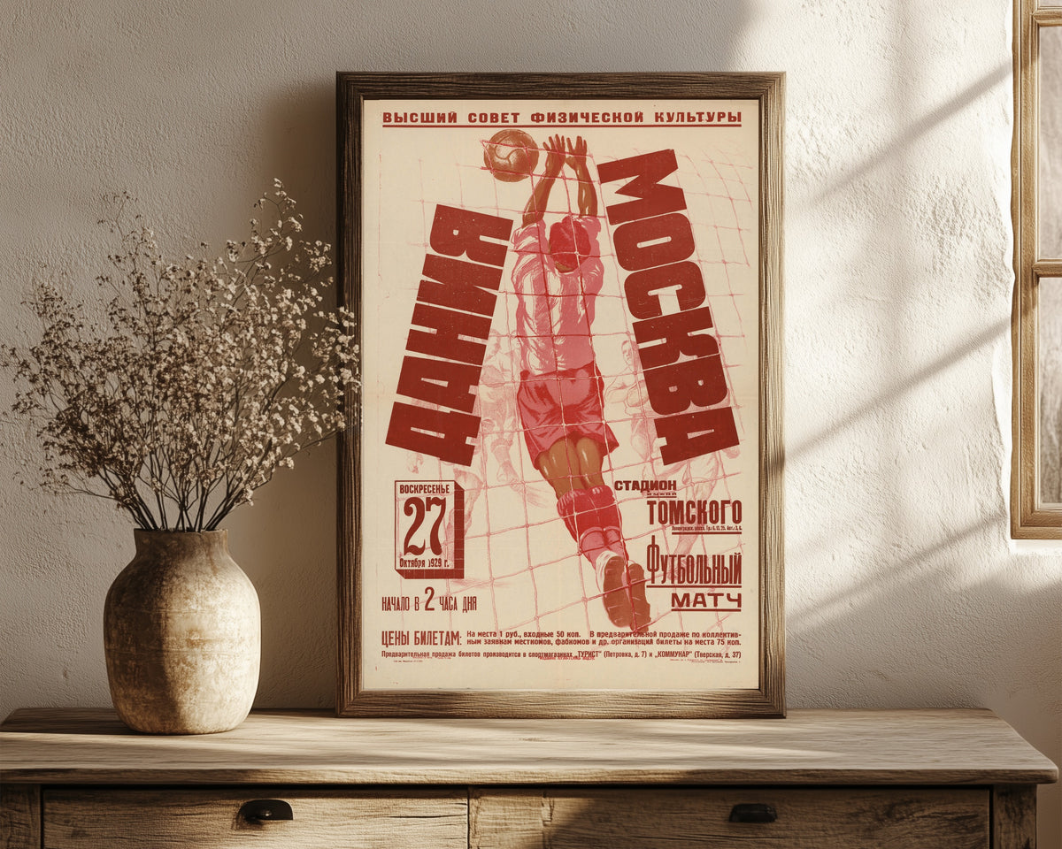 Framed art print of Denmark v. Moscow: Football Match, 1929, in a dark wood frame leaning on a rustic console beside dried flowers