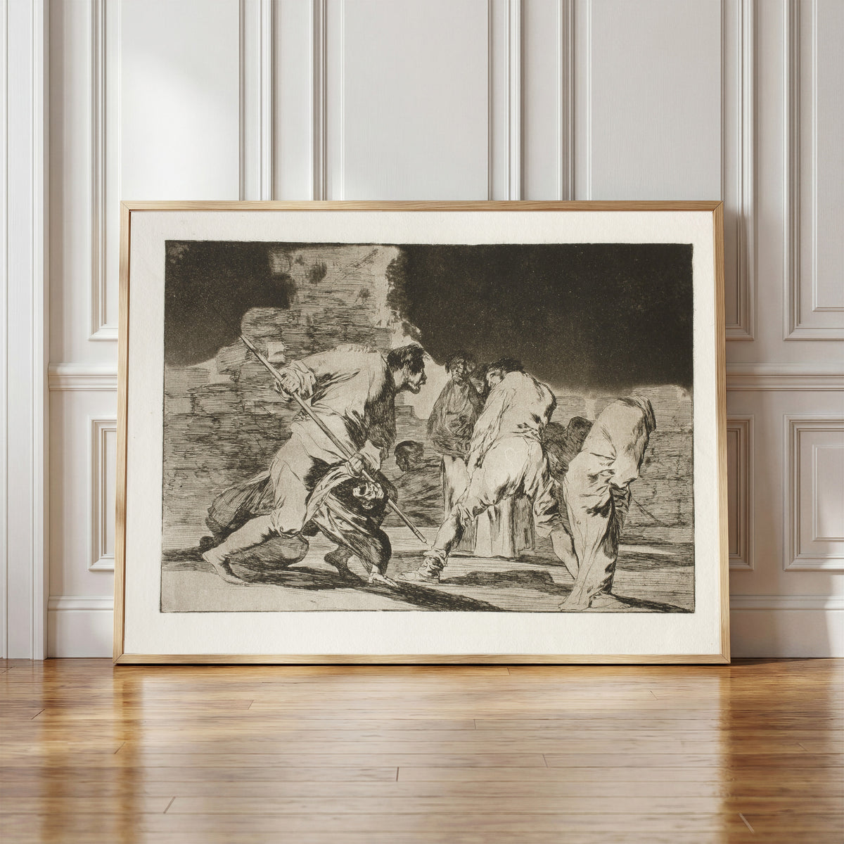 Framed art print of Disparate cruel (Cruel Folly), from Los Disparates by Francisco de Goya, in a light wood frame leaning against a panelled white wall