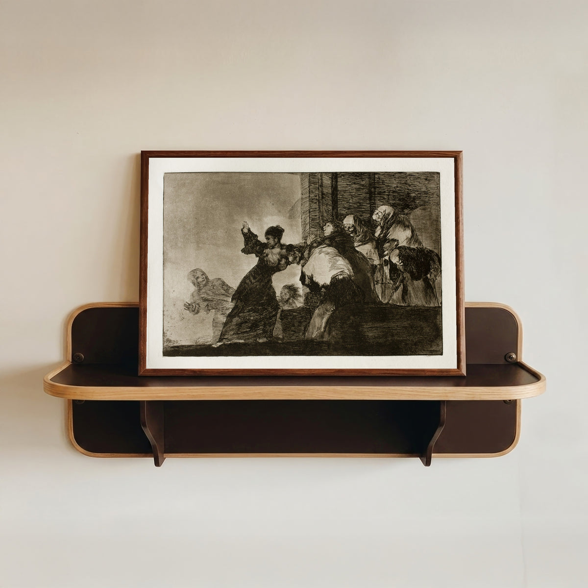 Framed art print of Disparate pobre (Poor Folly), from Los Disparates by Francisco de Goya, in a dark wood frame resting on a wall shelf