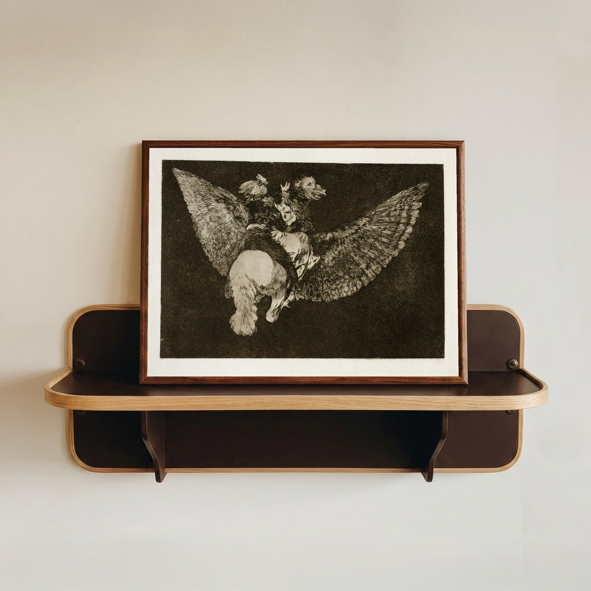 Framed art print of Disparate volante (Flying Folly), from Los Disparates by Francisco de Goya, in a dark wood frame resting on a wall shelf