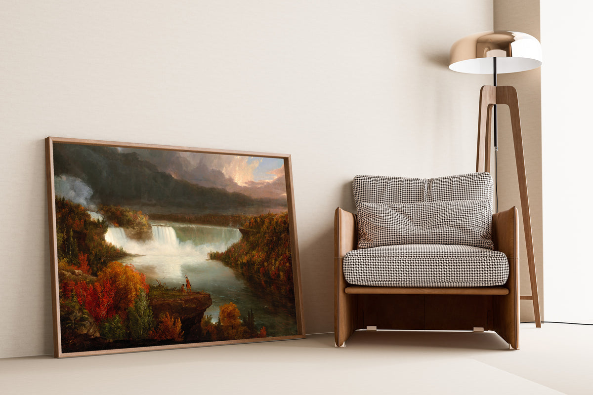 Distant View of Niagara Falls by Thomas Cole — framed and leaning against a wall beside an armchair and a floor lamp