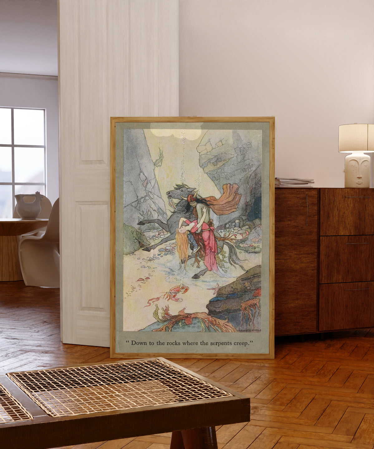 Framed art print of Down to the rocks where the serpents creep. by Warwick Goble, in a light wood frame leaning in a warm room with a parquet floor