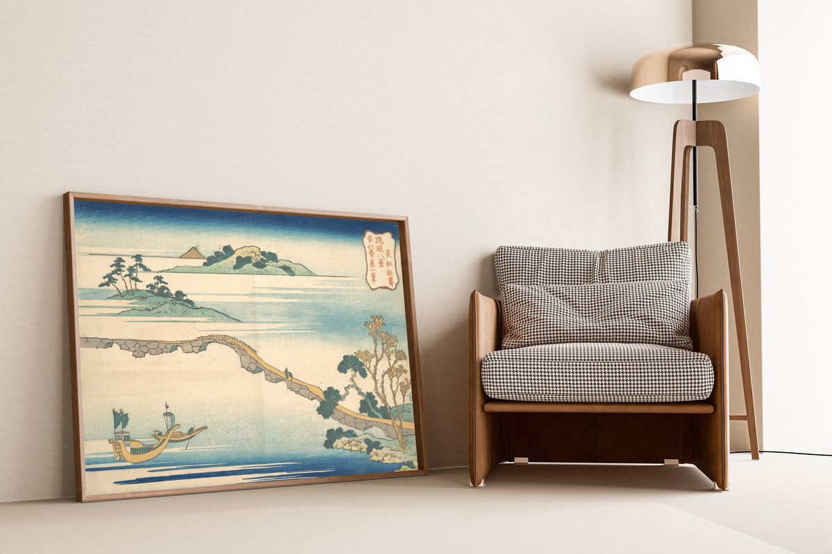 Framed art print of Eight Views of the Ryūkyū Islands: Autumn Sky at Chōkō by Katsushika Hokusai, leaning against a wall beside an armchair and a floor lamp