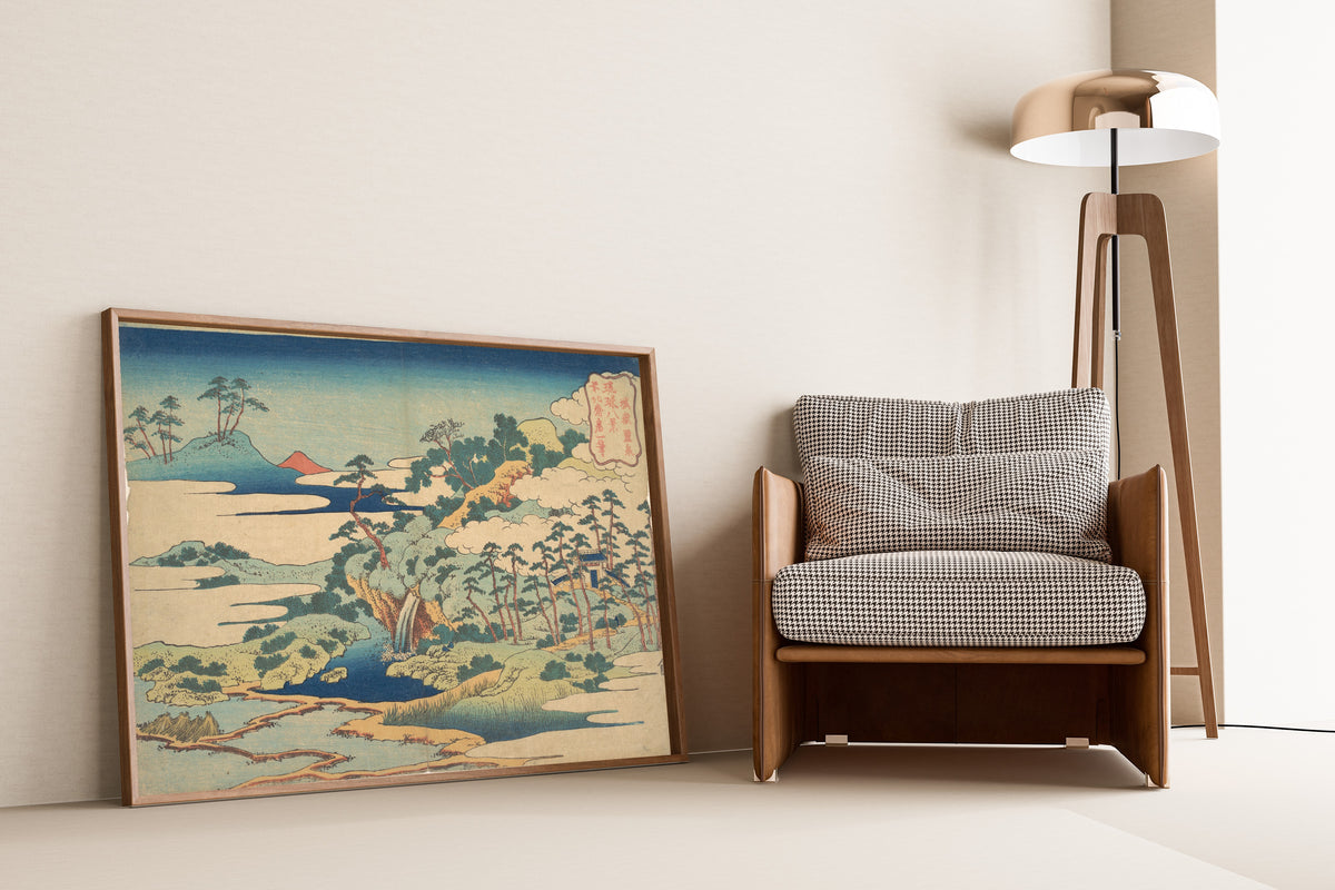 Framed art print of Eight Views of the Ryūkyū Islands: The Sacred Spring at… by Katsushika Hokusai, leaning against a wall beside an armchair and a floor lamp