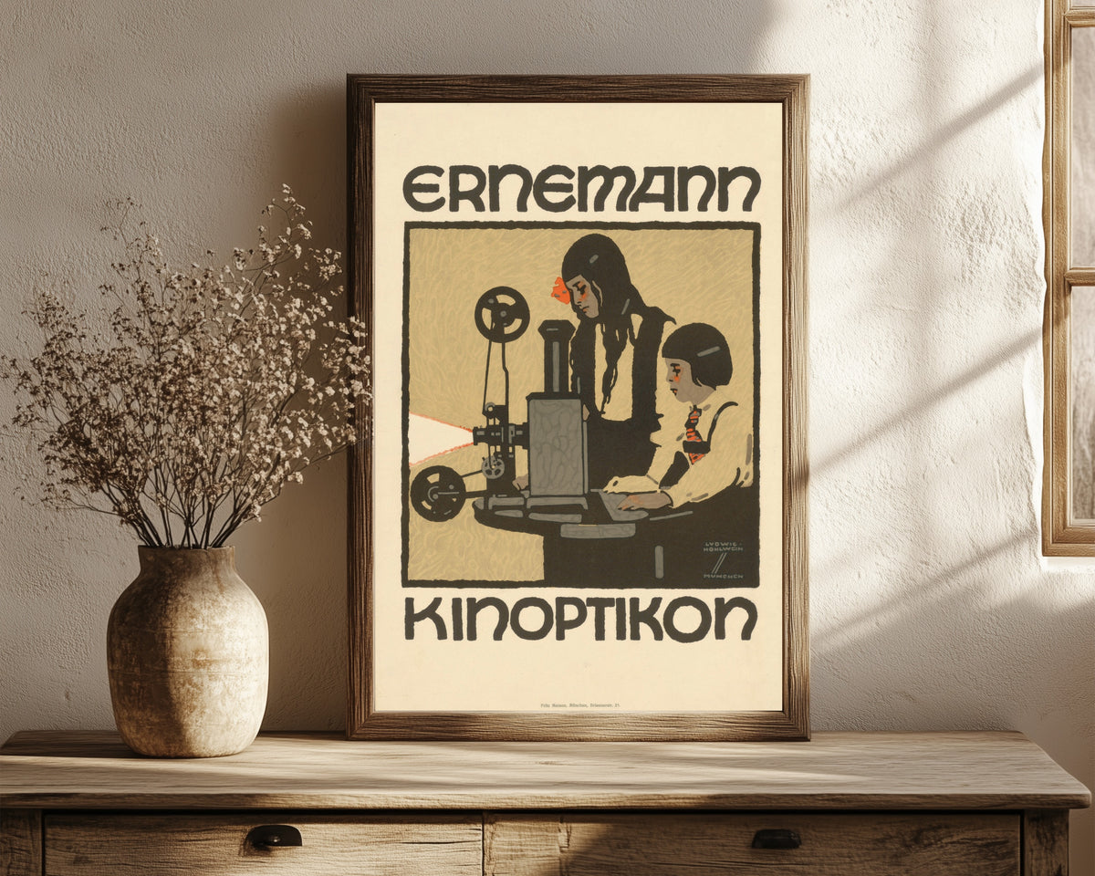 Framed art print of Ernemann Kinoptikon by Ludwig Hohlwein, in a dark wood frame leaning on a rustic console beside dried flowers