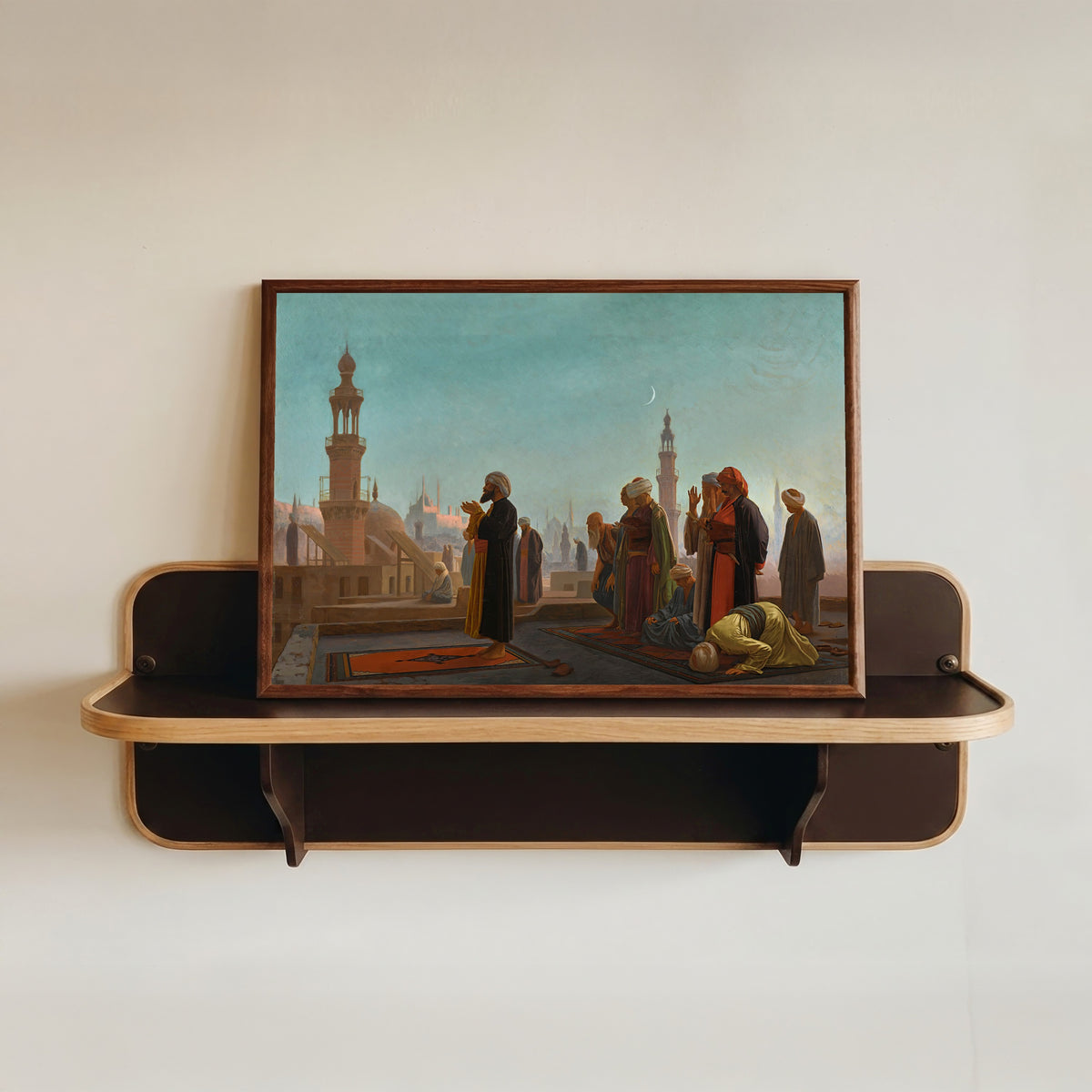 Framed art print of Evening Prayer, Cairo by Jean-Léon Gérôme, in a dark wood frame resting on a wall shelf