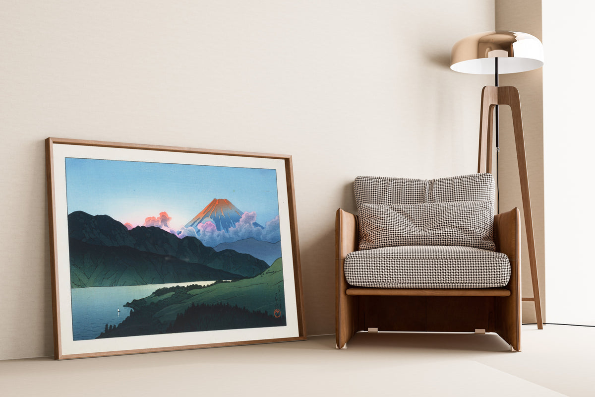 Framed art print of Evening of Mount Fuji from Lake Ashino-ko by Kawase Hasui, leaning against a wall beside an armchair and a floor lamp