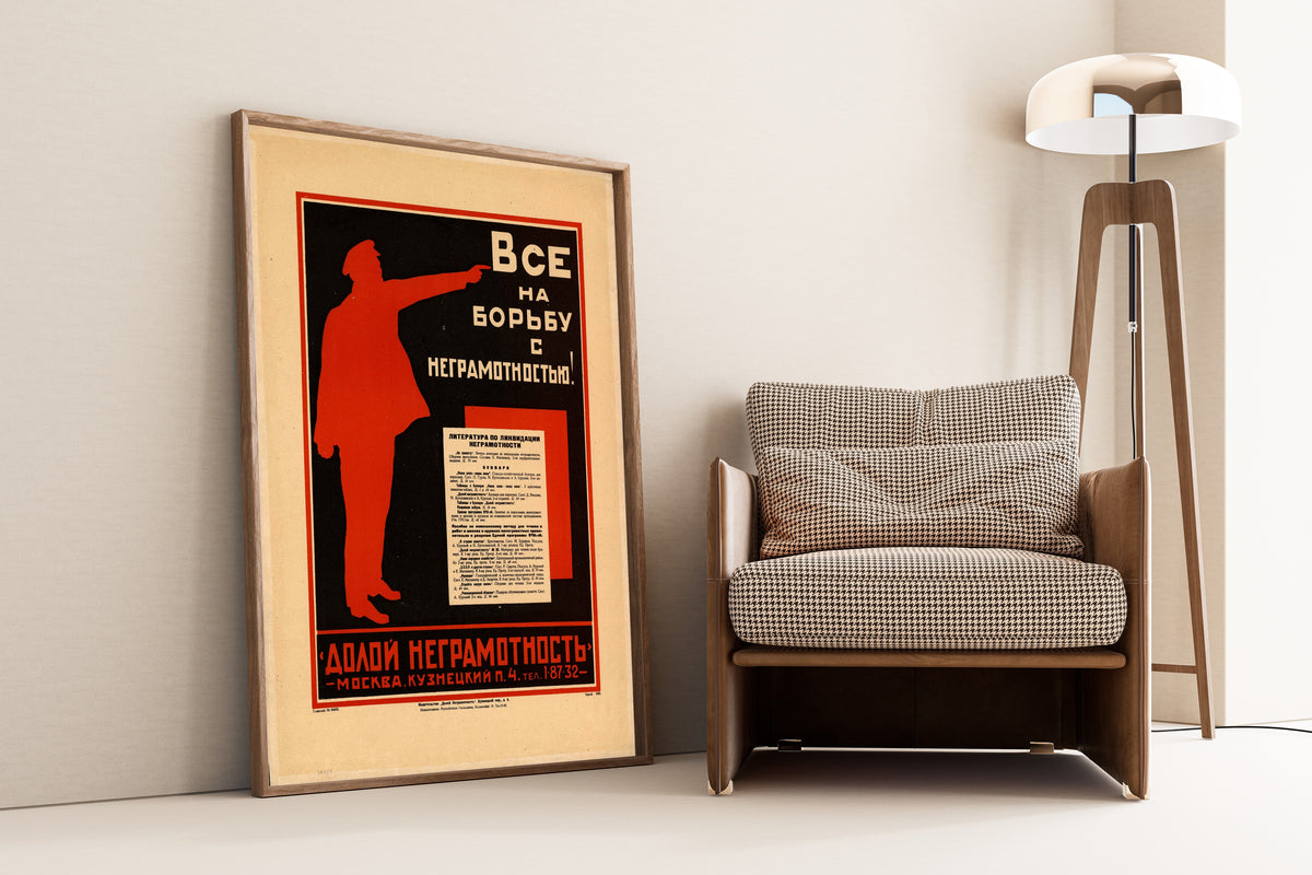 Framed art print of Everyone into the Fight Against Illiteracy!, leaning against a wall beside an armchair and a floor lamp
