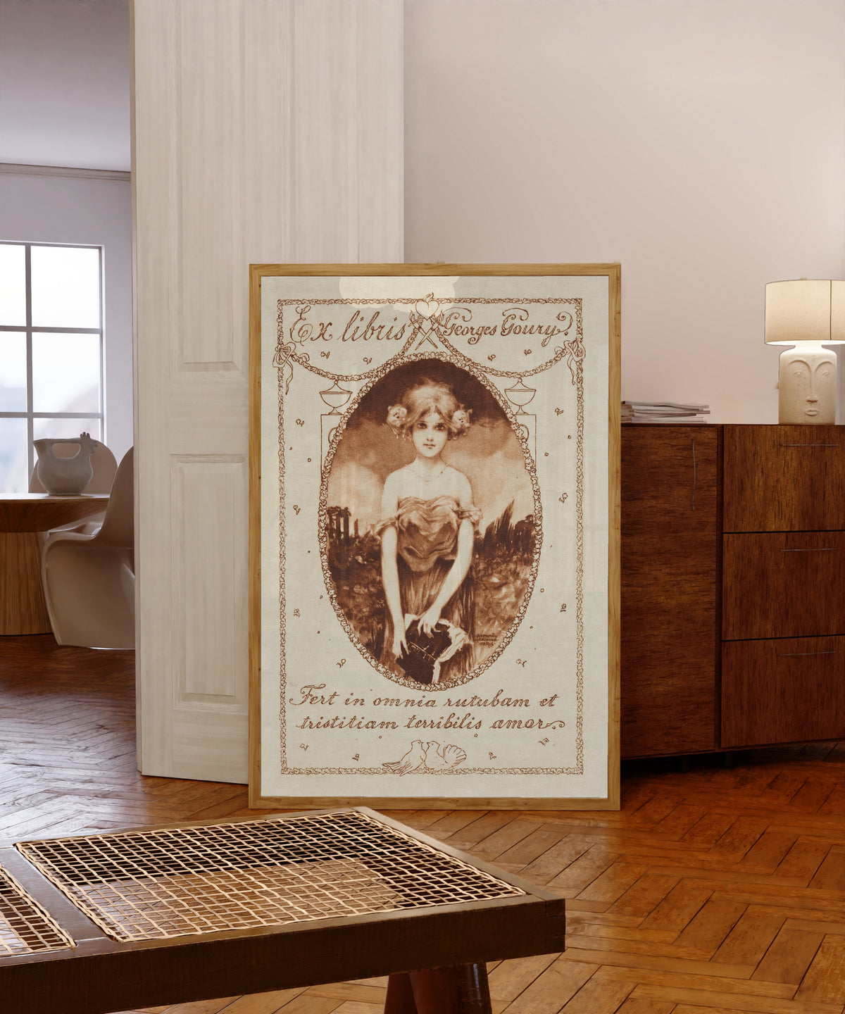 Framed art print of Ex Libris Georges Goury by Raphael Kirchner, in a light wood frame leaning in a warm room with a parquet floor