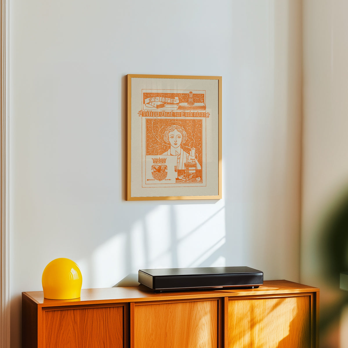 Framed art print of Ex Libris Philipp Graf zu Eulenburg by Joseph Sattler, in a light wood frame on a white wall above an orange sideboard
