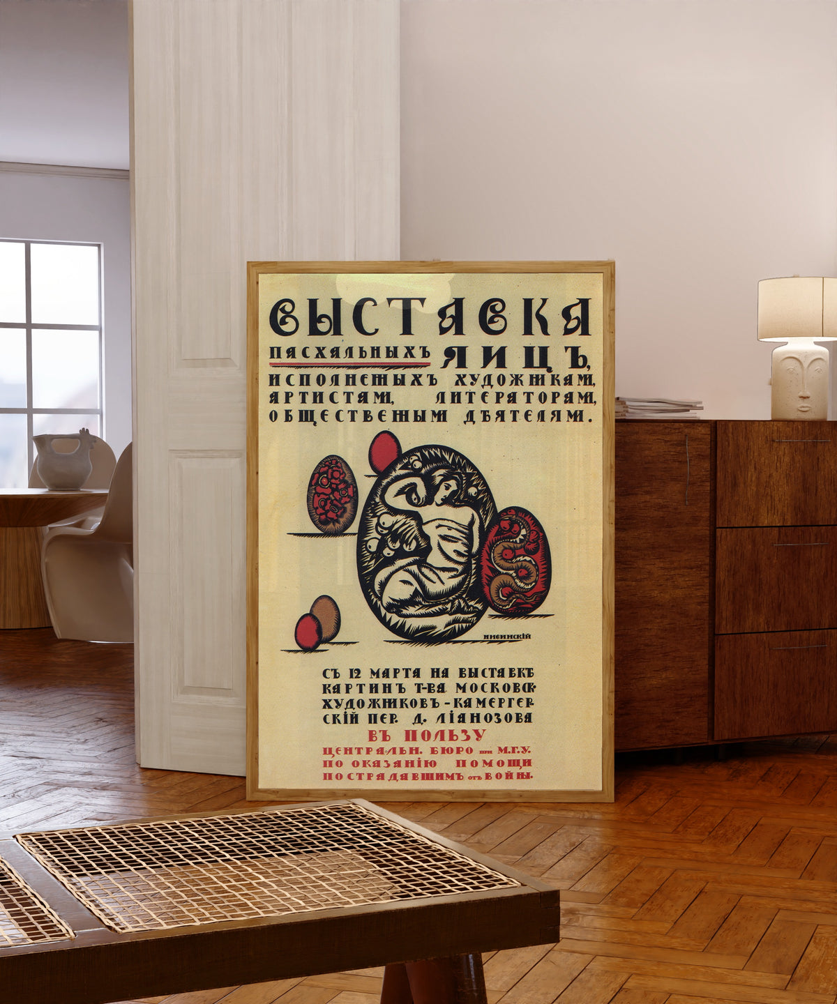 Framed art print of Exhibition of Easter eggs made by artists, actors… by Ignaty Nivinsky, in a light wood frame leaning in a warm room with a parquet floor