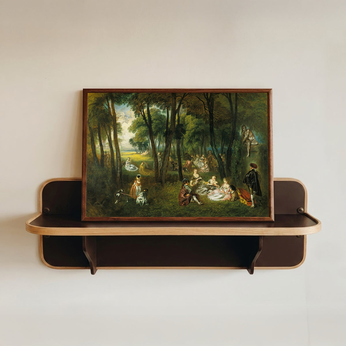 Framed art print of Fête galante in a Wooded Landscape by Jean-Antoine Watteau, in a dark wood frame resting on a wall shelf
