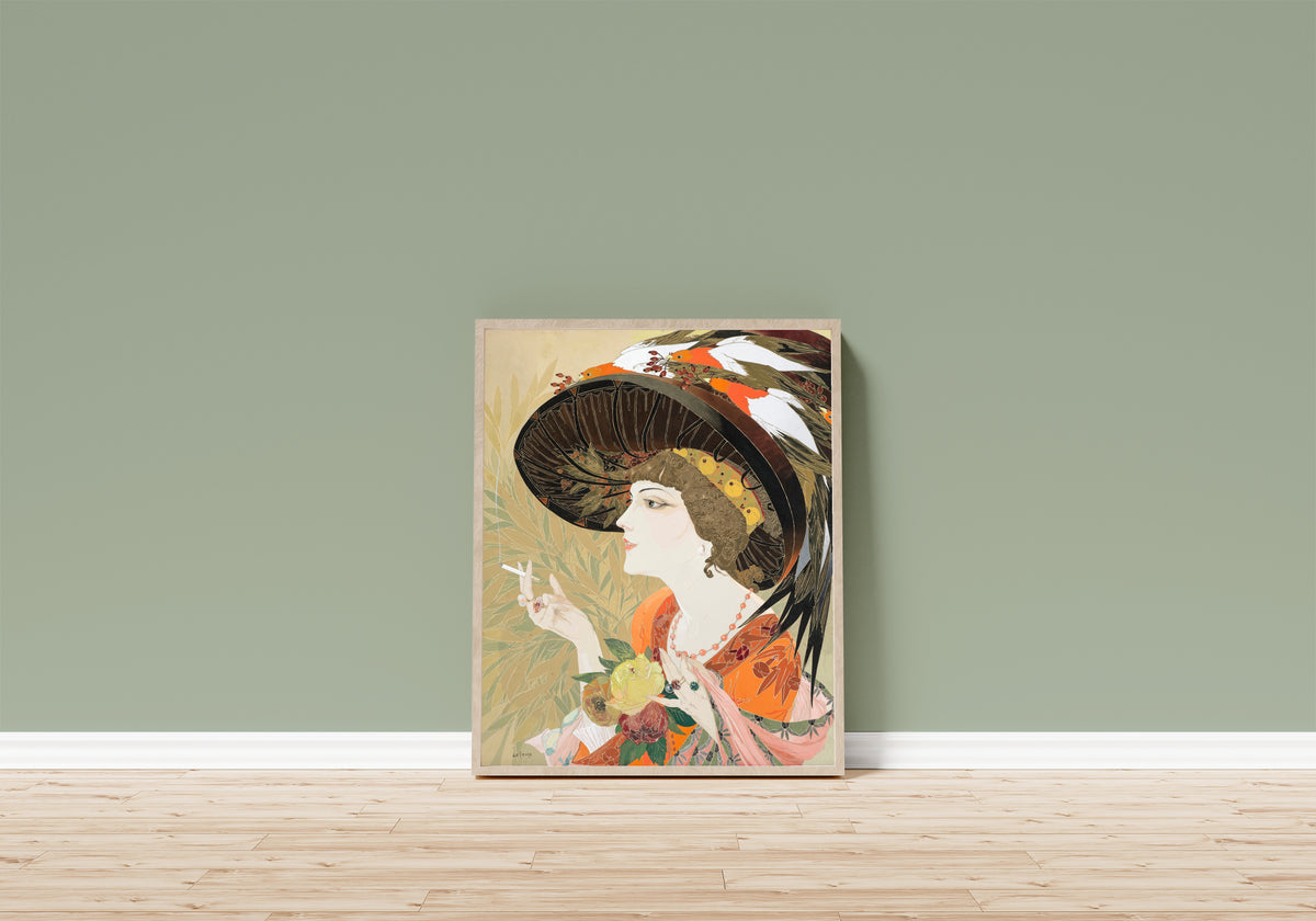 Framed art print of Femme en buste fumant de profil by Georges de Feure, in a light wood frame leaning on a sage green wall above a wooden floor