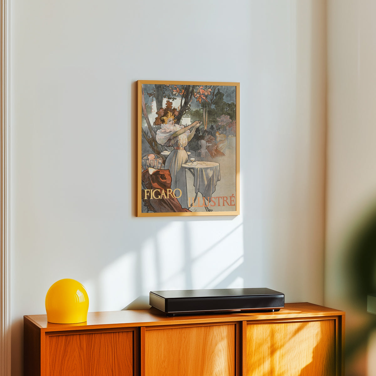 Framed art print of Figaro Illustré by Alphonse Mucha, in a light wood frame on a white wall above an orange sideboard