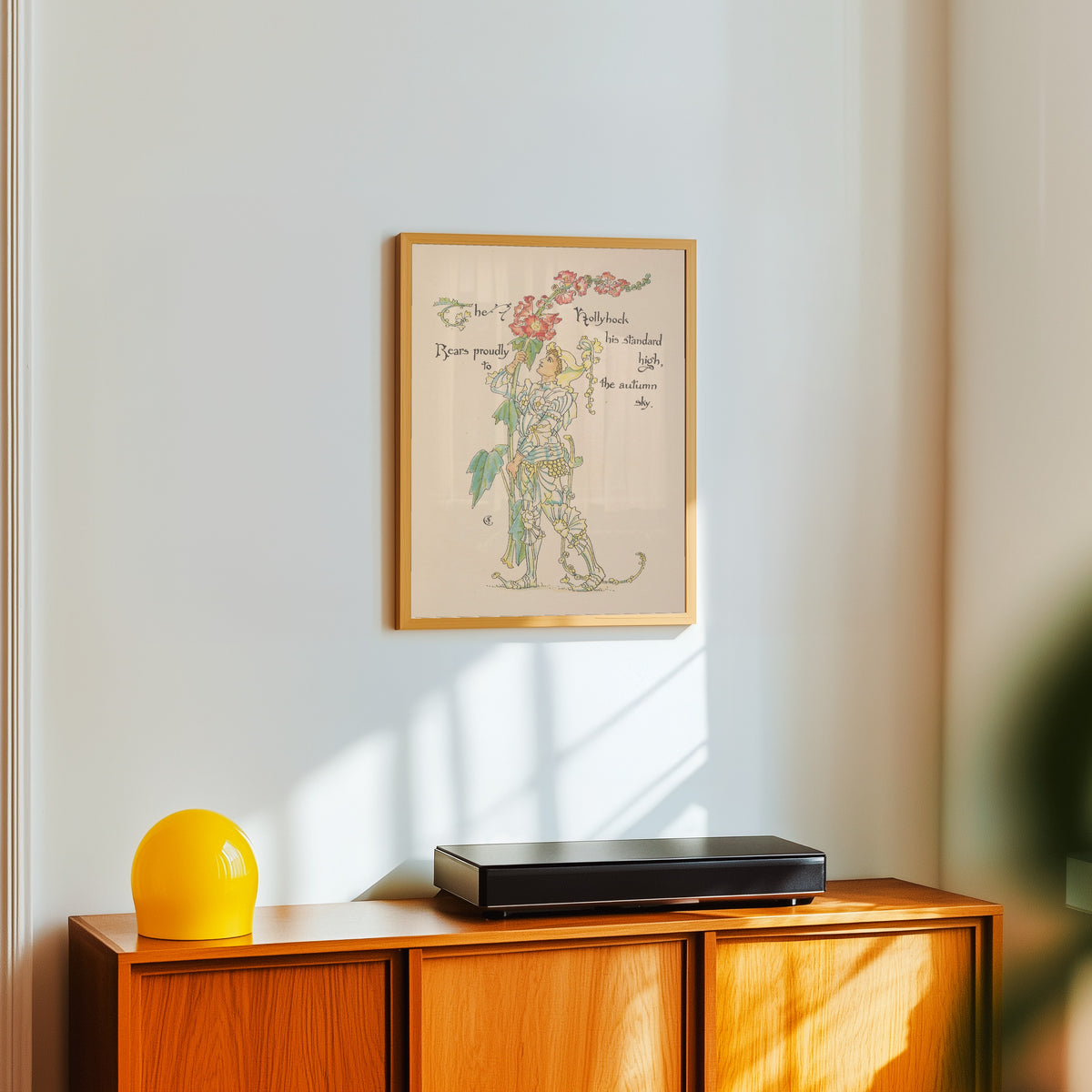 Framed art print of Flora's Feast: Hollyhock by Walter Crane, in a light wood frame on a white wall above an orange sideboard