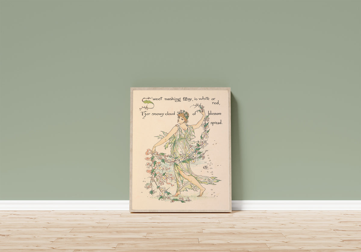 Framed art print of Flora's Feast: May by Walter Crane, in a light wood frame leaning on a sage green wall above a wooden floor