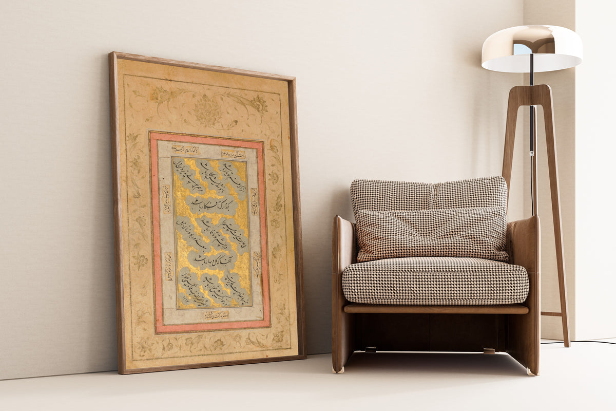 Framed art print of Folio with Verses in Nasta'liq Script by Mir `Imad al-Hasani, leaning against a wall beside an armchair and a floor lamp