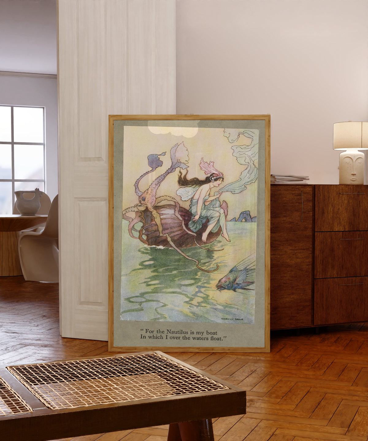 Framed art print of For the Nautilus is my boat in which I over the waters… by Warwick Goble, in a light wood frame leaning in a warm room with a parquet floor