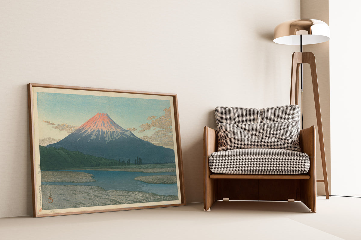Framed art print of Fuji River by Kawase Hasui, leaning against a wall beside an armchair and a floor lamp