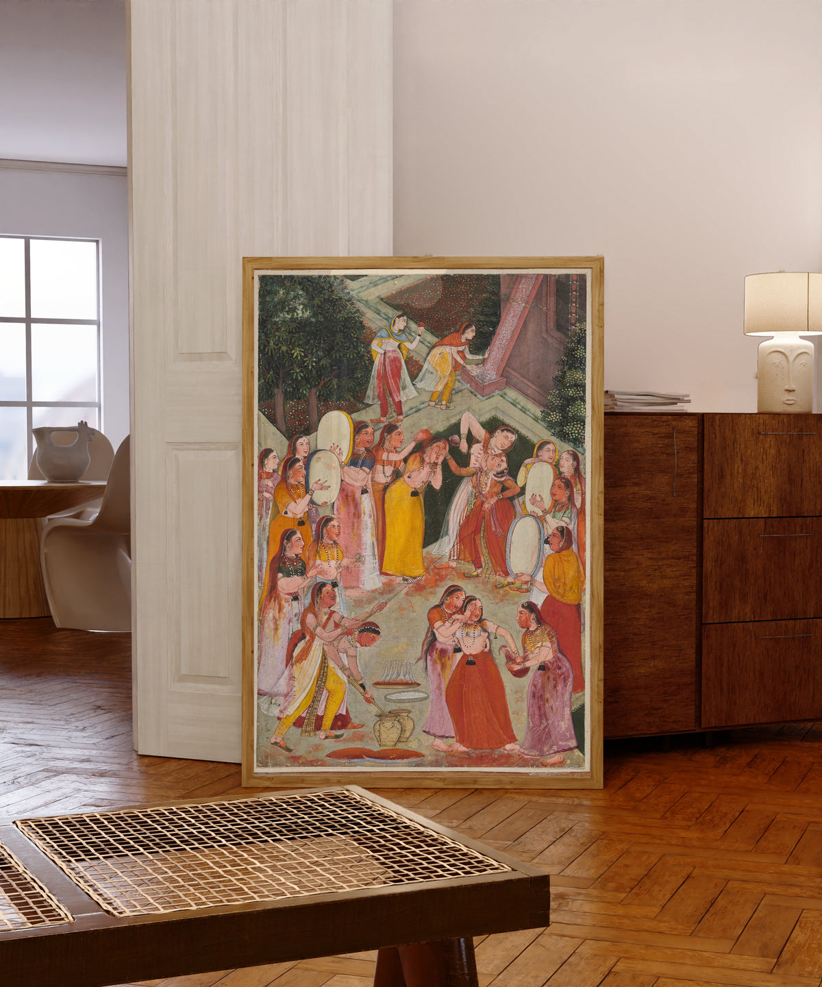 Framed art print of Girls Spraying Each Other at Holi by Bikaner school, in a light wood frame leaning in a warm room with a parquet floor