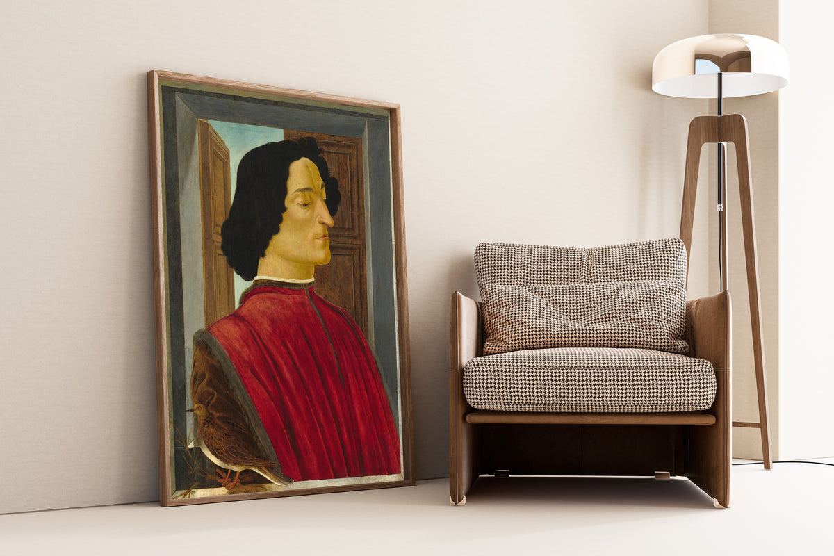 Framed art print of Giuliano de’ Medici by Sandro Botticelli, leaning against a wall beside an armchair and a floor lamp