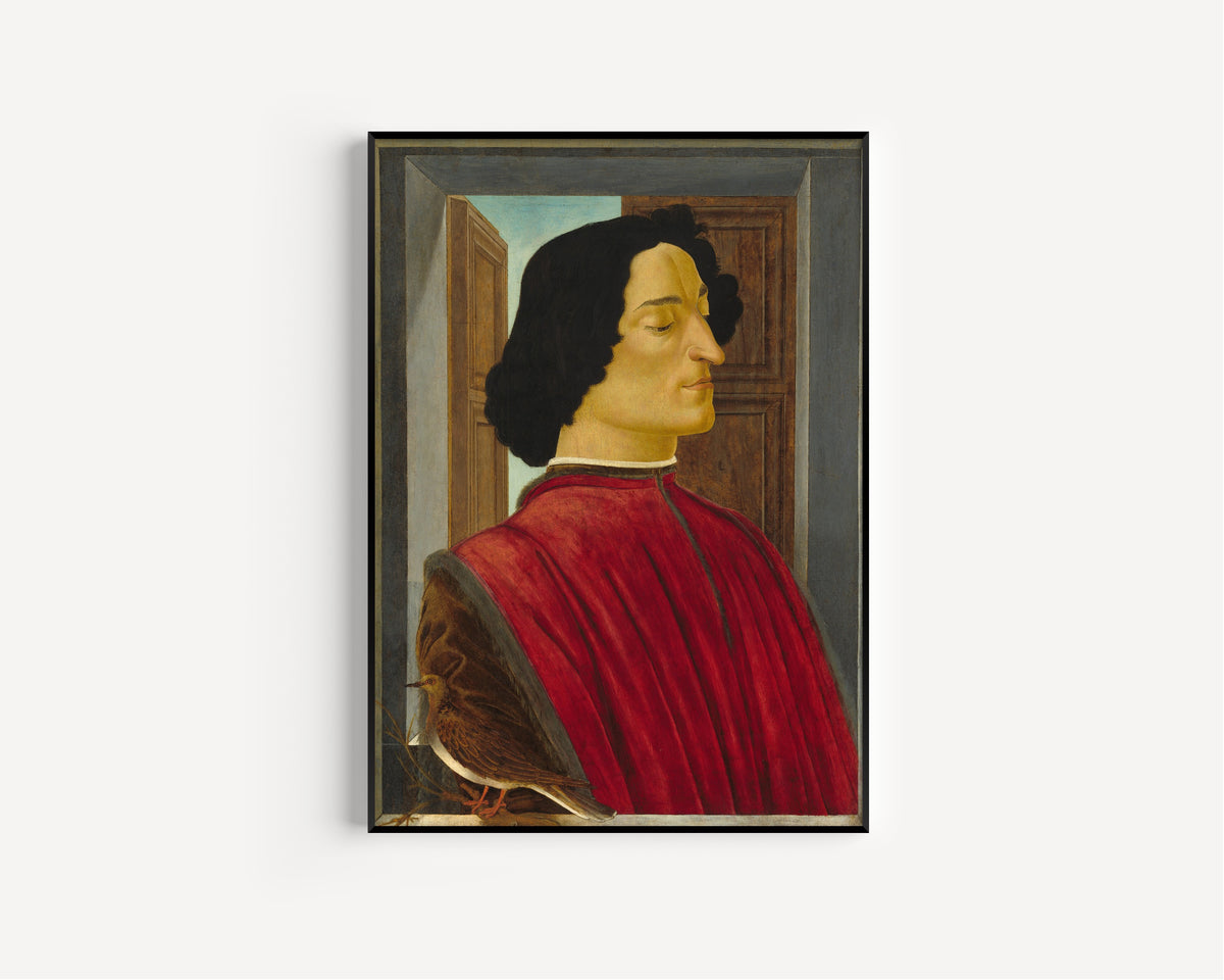 Framed art print of Giuliano de’ Medici by Sandro Botticelli, in a slim black frame on a plain white wall
